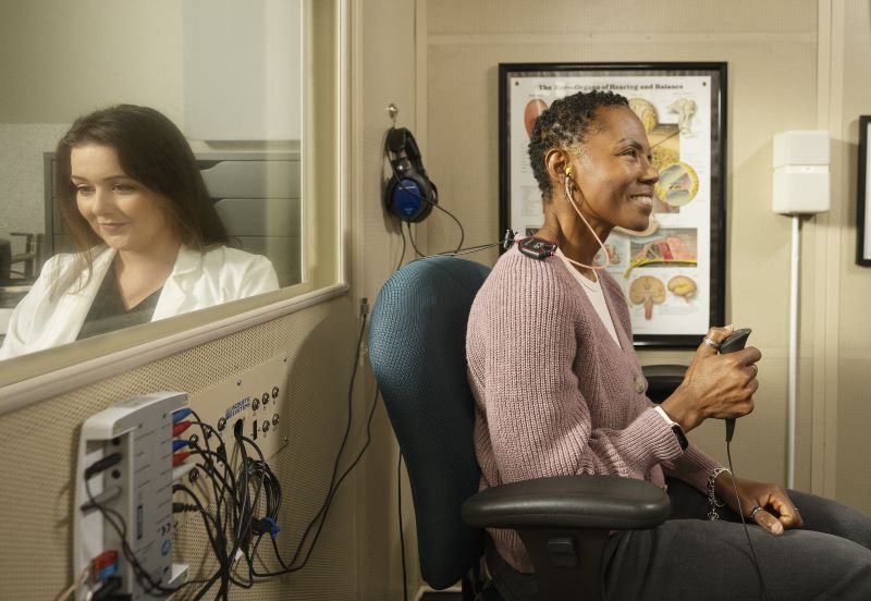 A woman sits in a sound-treated booth and receives a hearing test. 